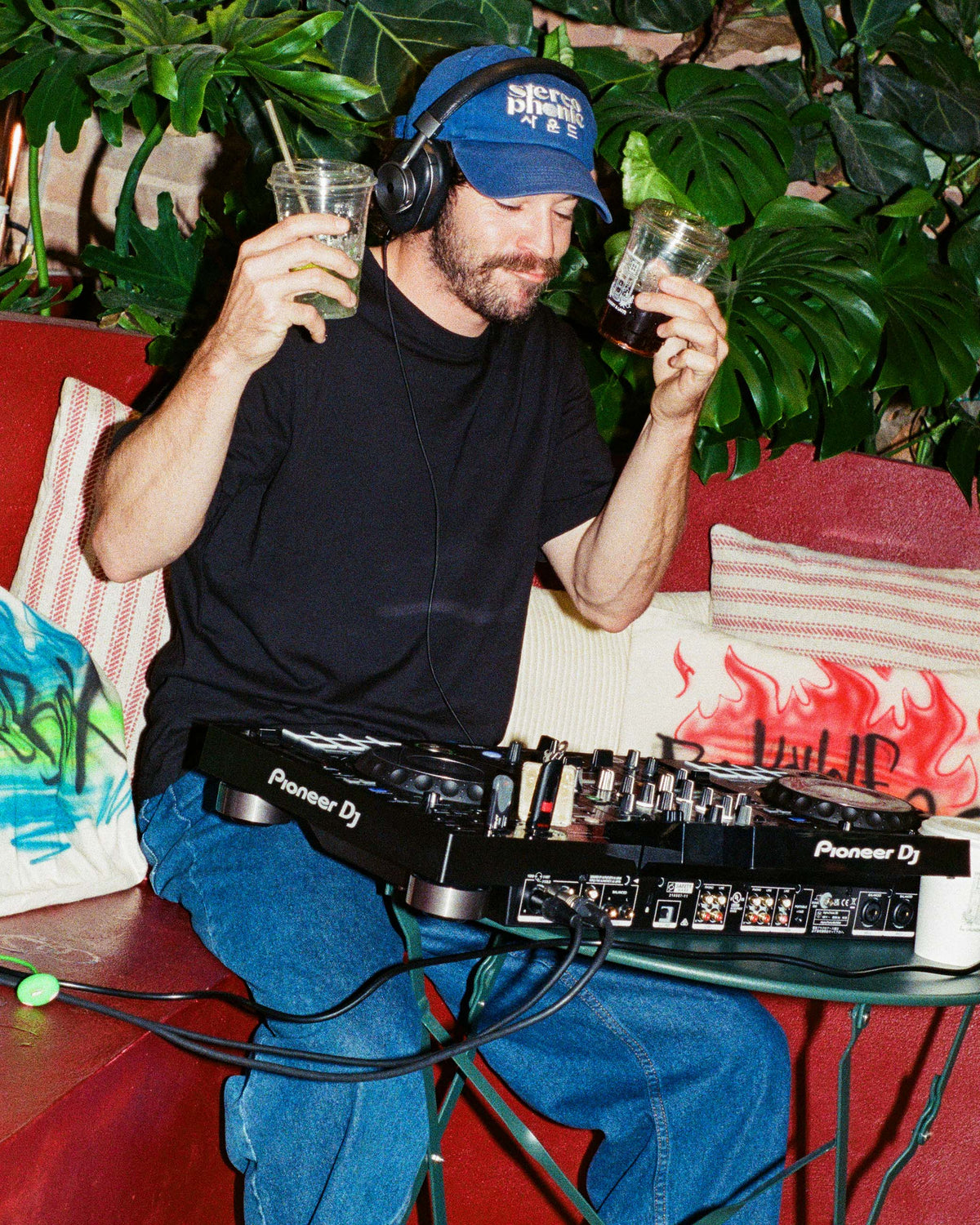 A DJ behind a mixer with two coffees in his hands enjoying the beats