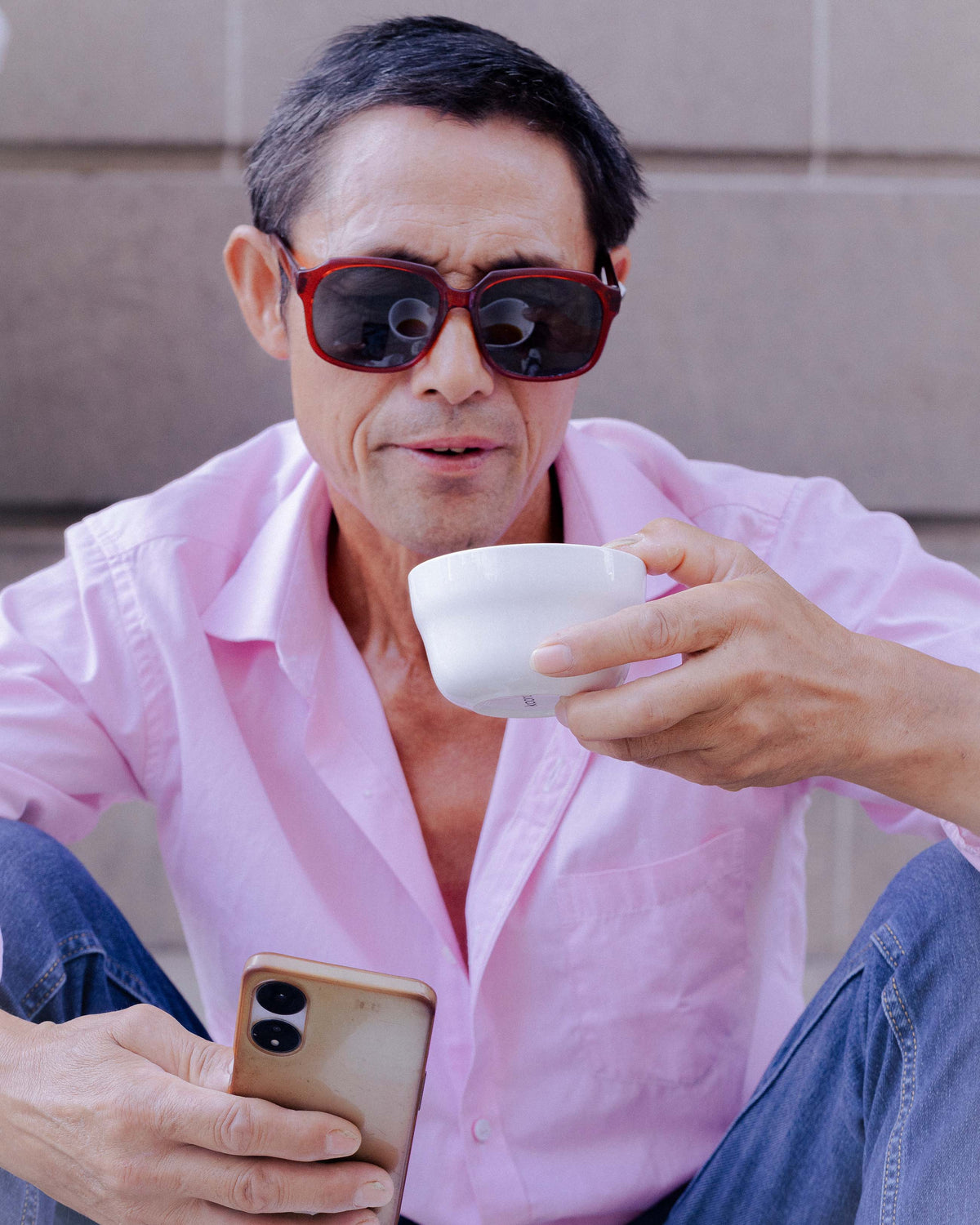 A man in a pink shirt holding a wide cup of coffee