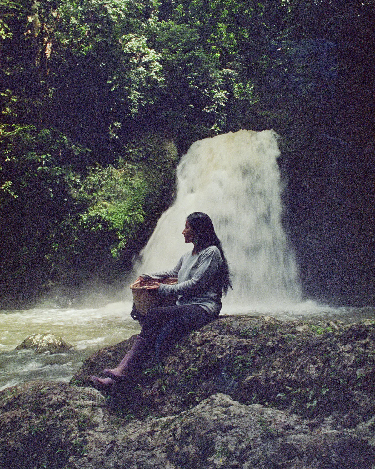 A woman sitting under a waterfall holding a basked of coffee cherries