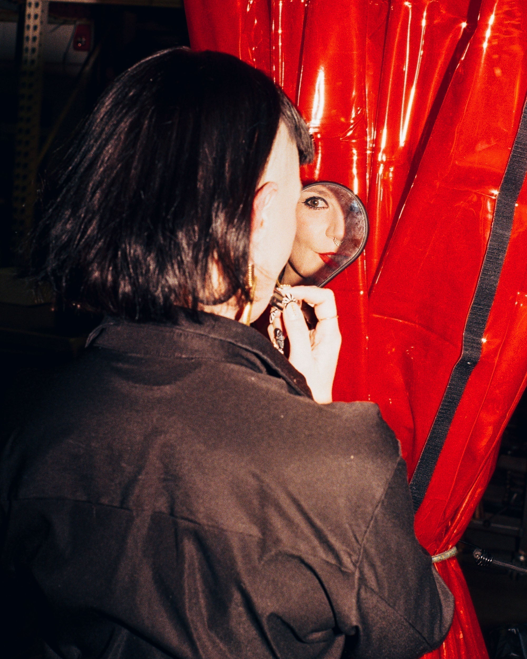 Rachel Apple looking into a mirror behind a red curtain